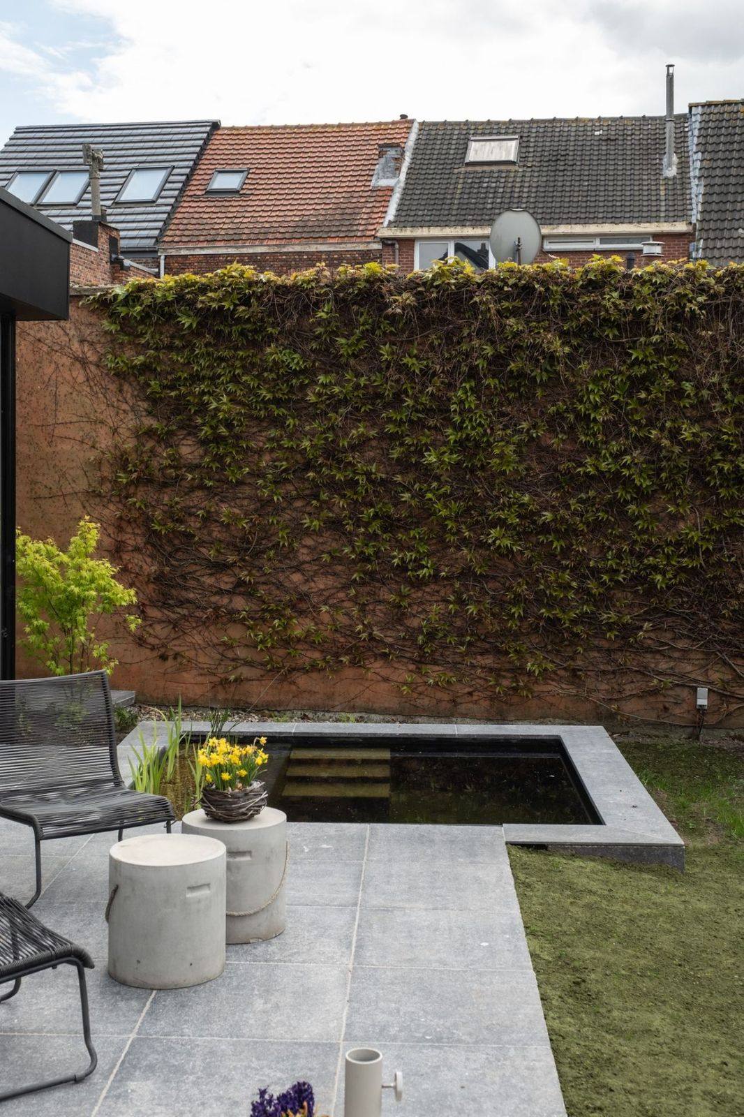 Stadstuin met spiegelvijver Stadstuin met strakke spiegelvijver, natuursteen terras en wijnrood begroeide muur